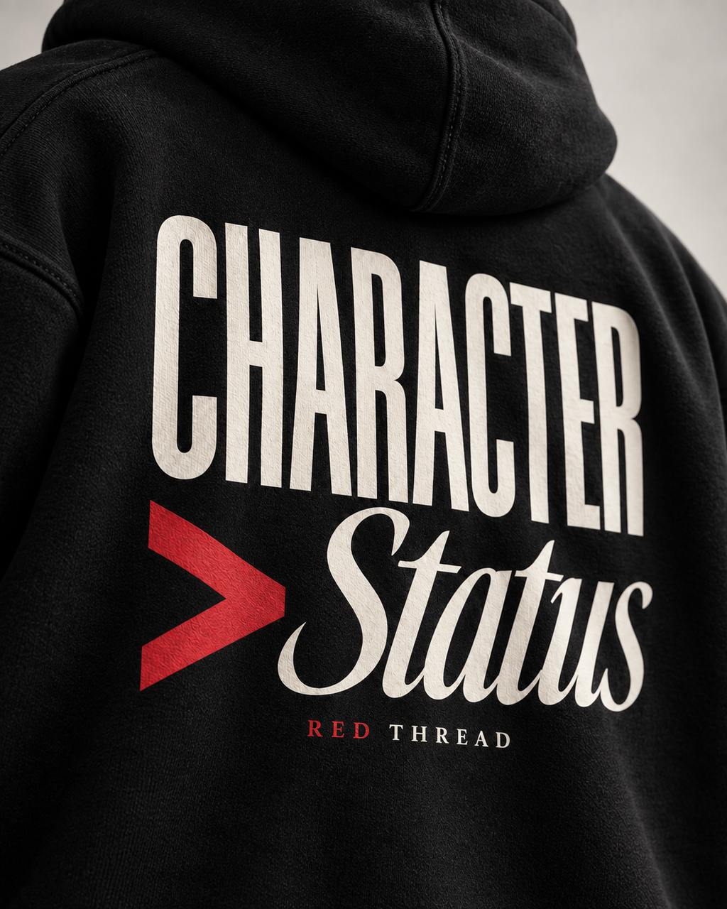Close-up of the back of a black hoodie featuring a large graphic print that reads 'CHARACTER > Status', with a red greater-than symbol and 'RED THREAD' in small red text below.